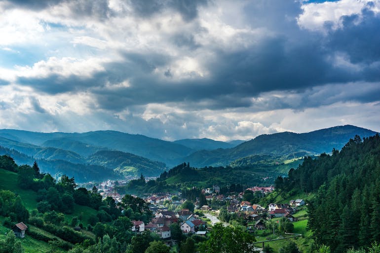 A small town sits in the majestic Carpathian mountains surrounded by beautiful forests on a cloudy day.