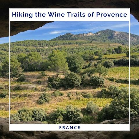 Wine country in Provence, France, is shown through a natural opening in a rock formation. Rolling greenery extends to the horizon, where there is blue sky.