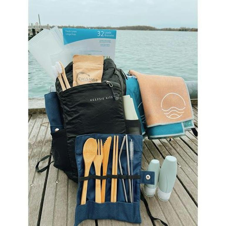 The Keepsie Kits Eco Explorers sustainable travel products kit, including a backpack, two towels, two toothbrushes, silicone bottles, laundry strips, bamboo cutlery, and more.