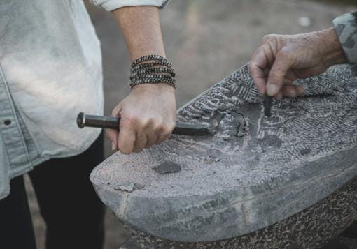 Two hands holding metal tools sculpt a soap stone together in Portugal, etching little designs on it.