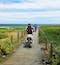 2 bikers cycle along a wooden boardwalk near the Atlantic Coast in northern Portugal under a sunny yet cloudy sky.